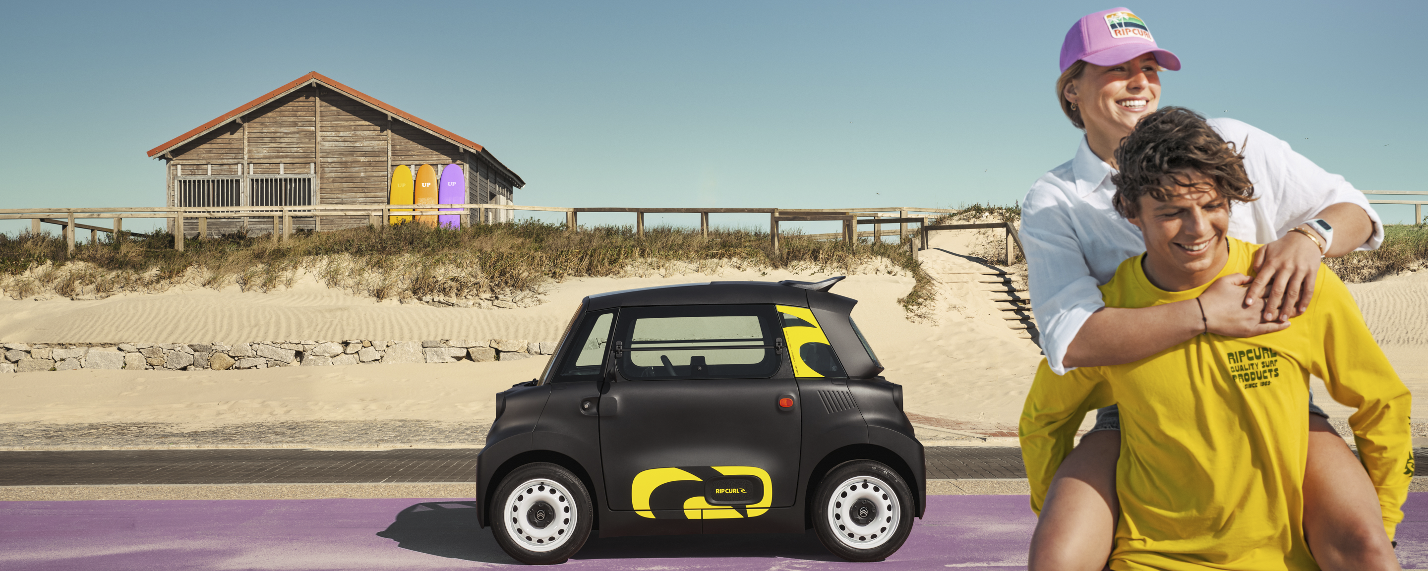 Vue latérale lifestyle de la Citroën Ami x Rip Curl électrique sans plaque d'immatriculation, liberté en bord de mer pour la Citroën Ami, voiture électrique urbaine
